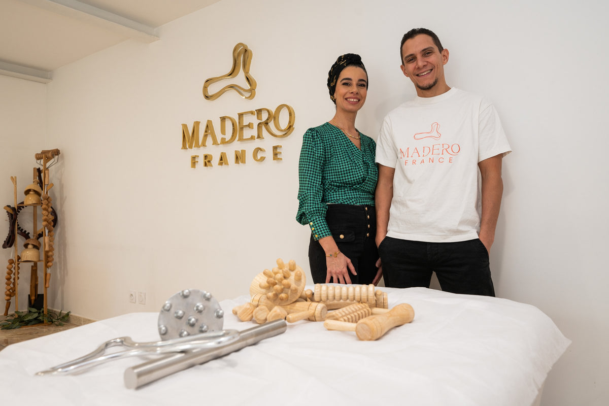 Chafia et Mehdi dans la salle de formation MADEROFRANCE, devant le logo doré, les outils posés sur la table de soin
